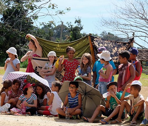 Kinder sitzen mit Regenschirmen vor der Sonne beim FSJ in Brasilien