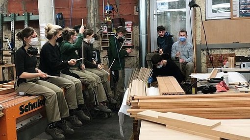 Freiwillige sitzen auf Tischen in einer Holzwerkstatt beim FSJ in Kassel