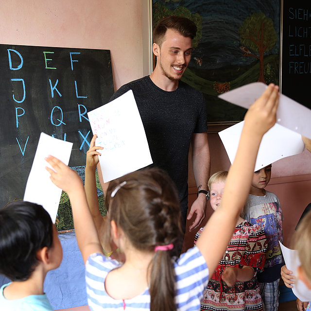 Kinder bestürmen Freiwilligen mit ihren Hausuafgaben im FSJ in der Schule