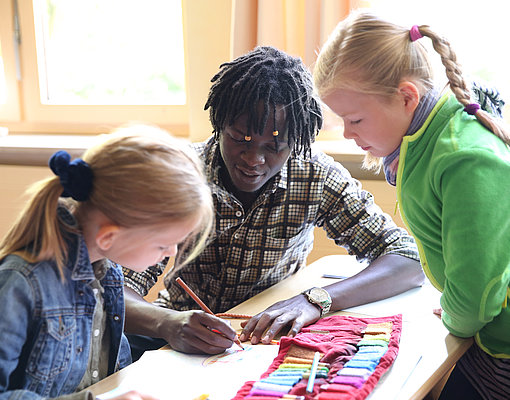 Freiwillger hilft Mädchen bei den Aufgaben im FSJ in der Schule