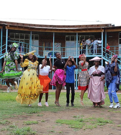 Mädchen in bunter Kleidung springen vor einer Schule in Namibia.