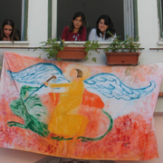 Waldorfschulen Südeuropa Kinder schauen aus Fenstern unter denen eine bunt bemalte Flagge hängt.