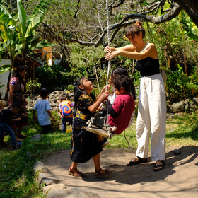 Waldorfschule Guatemala Drei Kinder auf Baum-Schaukel und eine Frau hilft ihnen